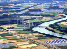 An aerial image showing agricultural lands with lots of solar power, windmills, high ways and a river (AI-generated by DALL·E)
