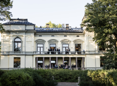 Bilde av Akademiets hus sett fra hagen, med mennesker på balkongen.