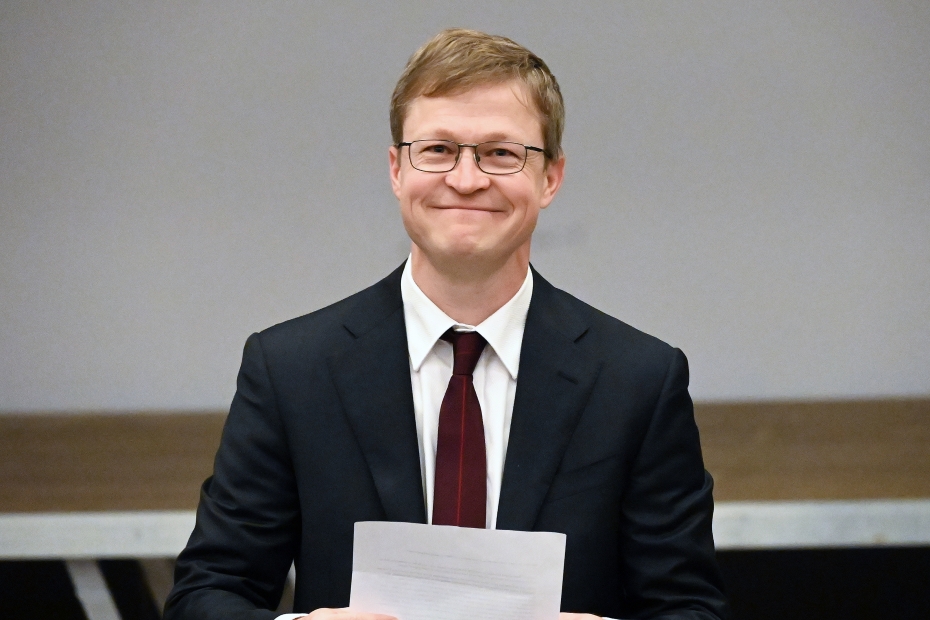 Man in a dark navy suit with a red tie smiling 