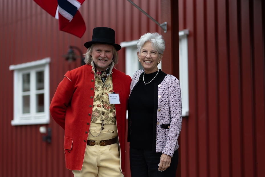 Hans-Olav Solli i bunad poserer med Cynthia Friend foran et rødt trehus