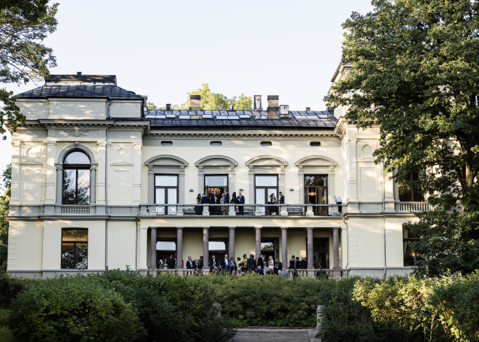 Bilde av Akademiets hus sett fra hagen, med mennesker på balkongen.